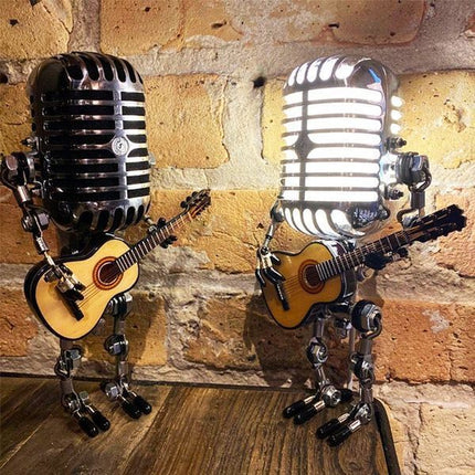 Two retro microphone robot desk lamps, one lit, playing guitars against a brick wall.