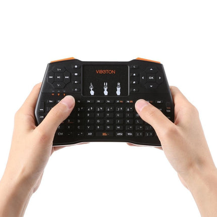 Hands hold a black wireless mini keyboard with a touchpad and media controls.