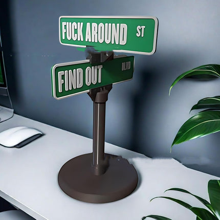 A desk decoration featuring two green street signs, one reading "FUCK AROUND ST" and the other "FIND OUT BLVD".
