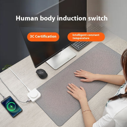A person's hands rest on a gray heated mouse pad with a human body induction switch.