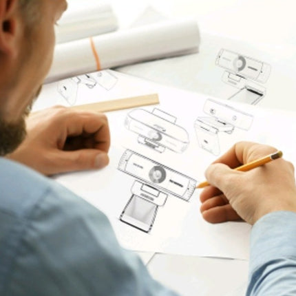 A person sketches various designs of a black USB webcam with a built-in microphone.