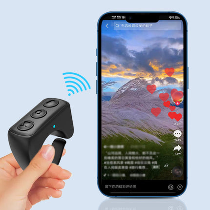 A hand holds a black Bluetooth remote ring, controlling a smartphone displaying a video.
